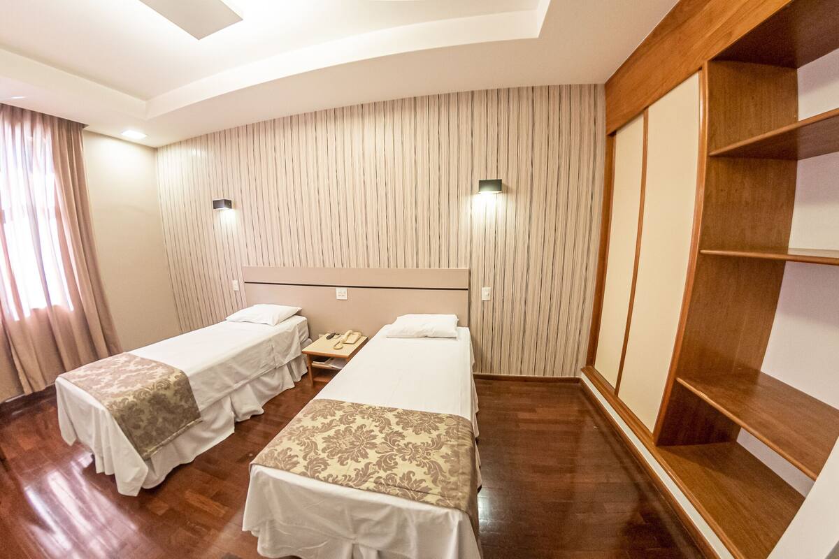 Habitación de hotel con dos camas, suelo de madera, armario empotrado y una lámpara en el techo.
