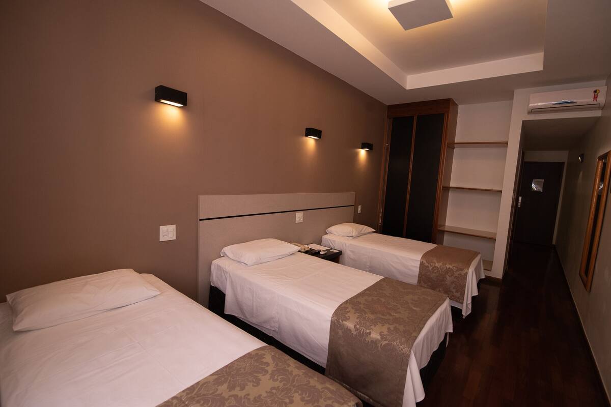 Habitación de hotel con tres camas, un armario de madera y un pasillo que conduce a una puerta.
