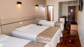 A hotel room with three single beds, wooden flooring, a flat-screen TV mounted on the wall, and an air conditioning unit.