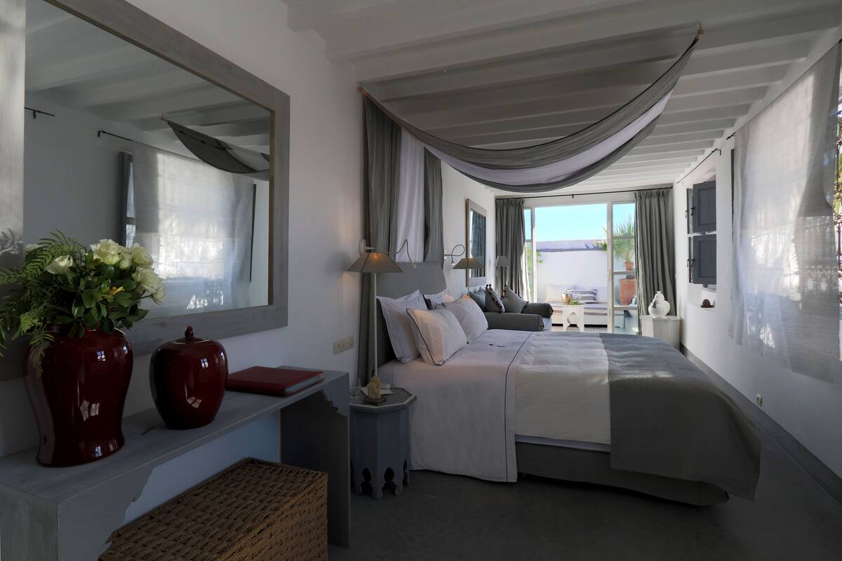 A modern bedroom with a large bed, bedside tables, a mirror, and a view of the outdoors.