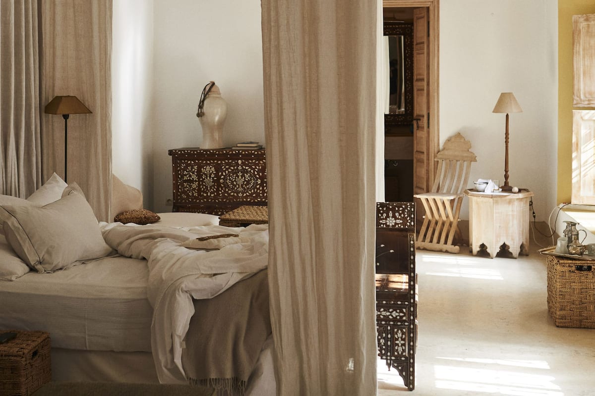 A room with a bed, a nightstand, a lamp, a chair, and a wicker basket.