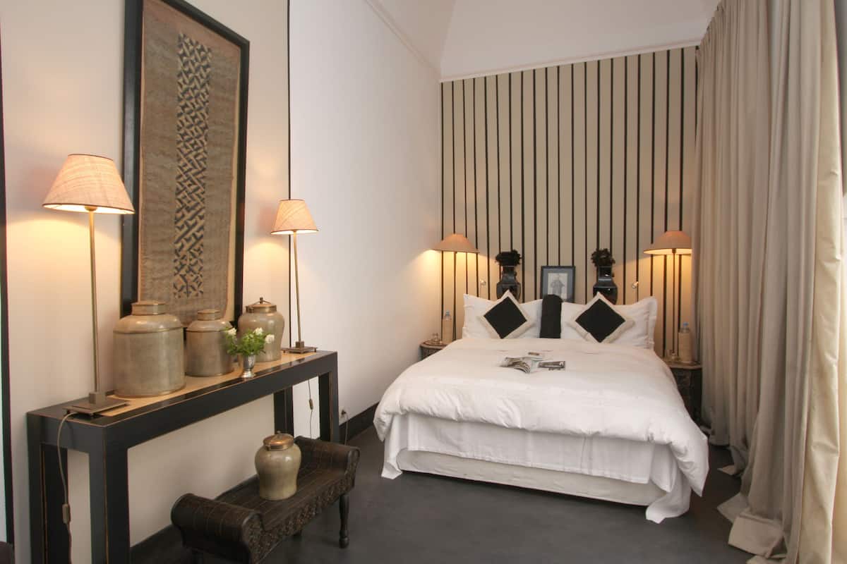 A neatly arranged bedroom with a large bed, bedside lamps, a console table with decorative items, and a framed artwork on the wall.