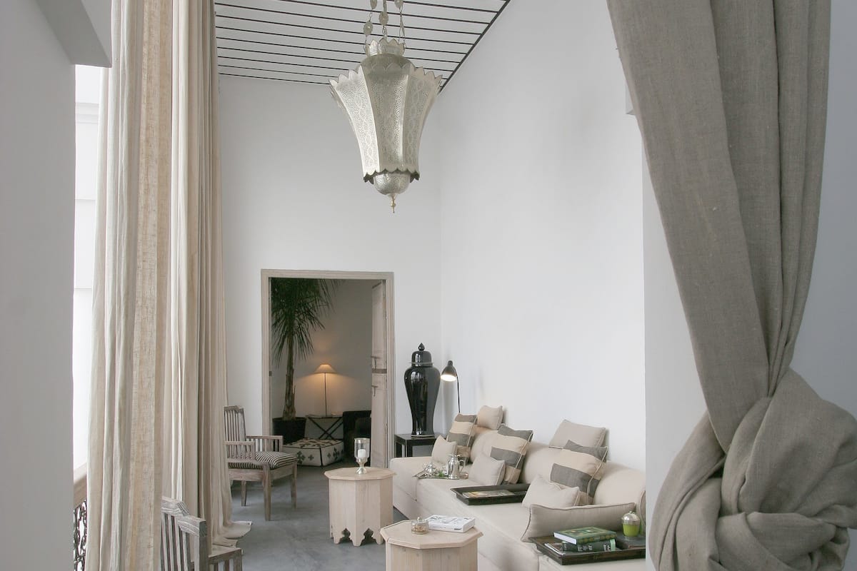 A modern living room with a sofa, a wooden chair, a small table, and a hanging light fixture.