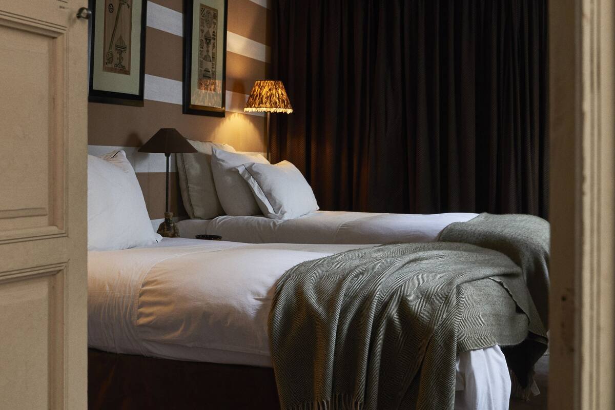 A hotel room with two beds, striped walls, a ceiling fan, an air conditioning unit, and framed artwork on the wall.