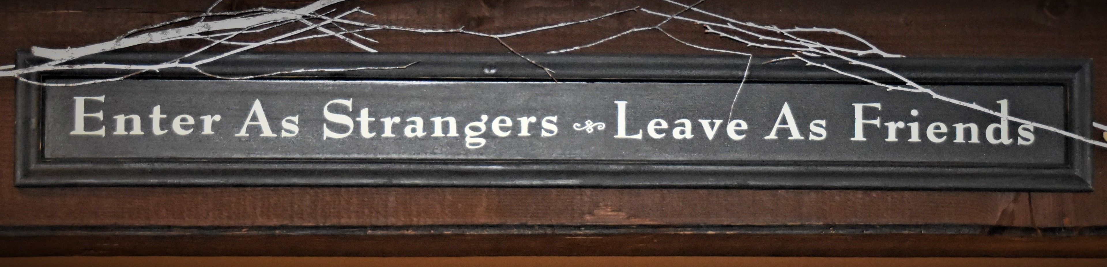 A sign with the text "Enter As Strangers, Leave As Friends".