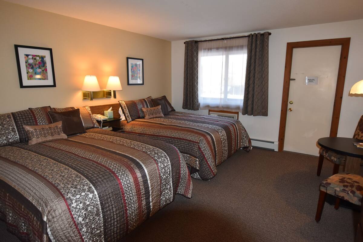 A hotel room with two beds, a desk, a chair, and two wall-mounted lamps.