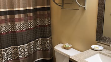 A bathroom with a patterned shower curtain, a toilet, a towel rack with folded towels, a soap dish, and a mirror.