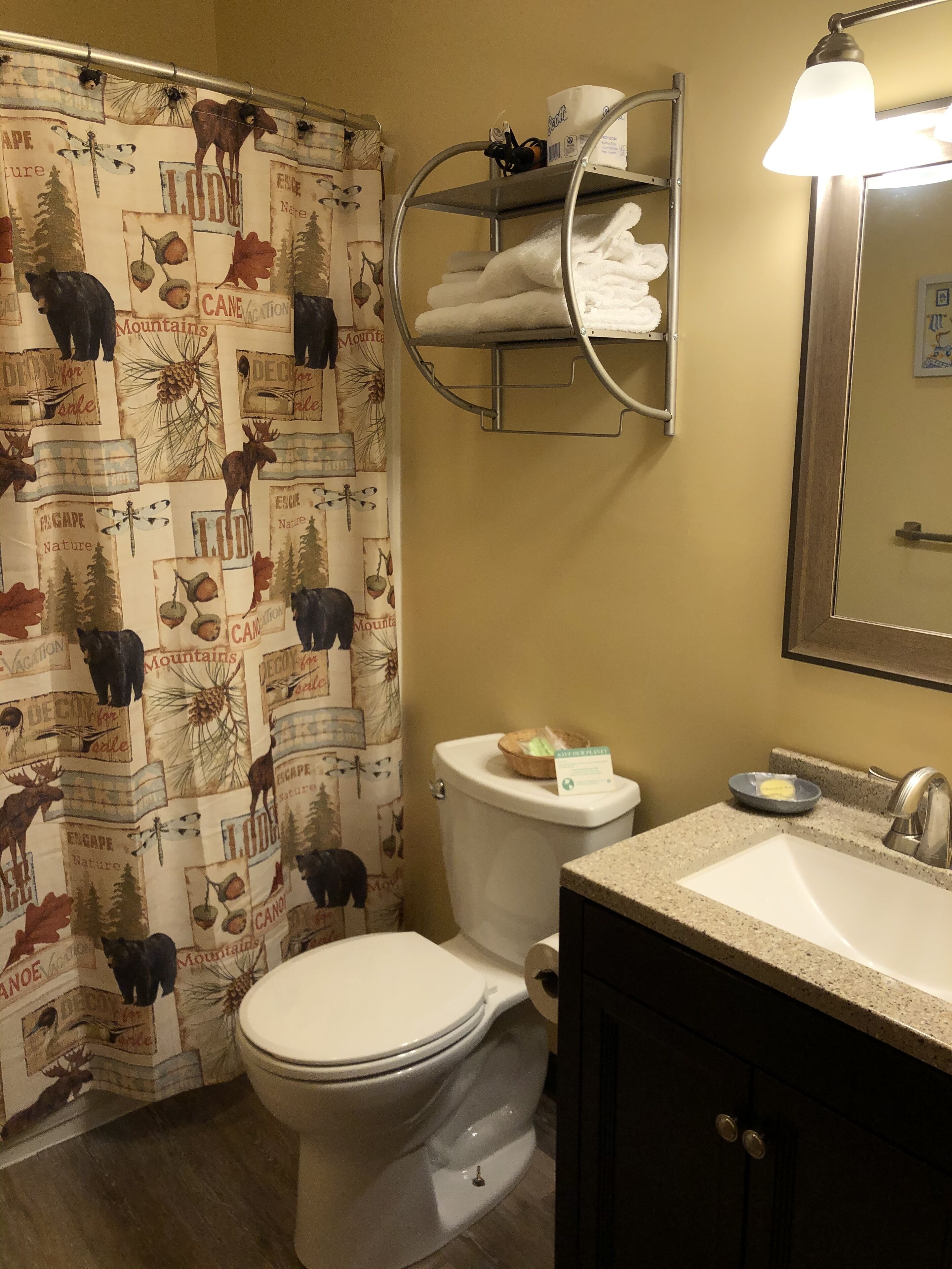 A bathroom with a toilet, sink, and a shower curtain with a nature-themed design.