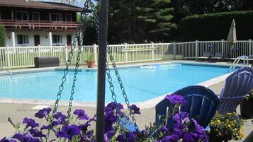 Une piscine entourée d’une clôture blanche, avec une chaise et des fleurs violettes au premier plan.