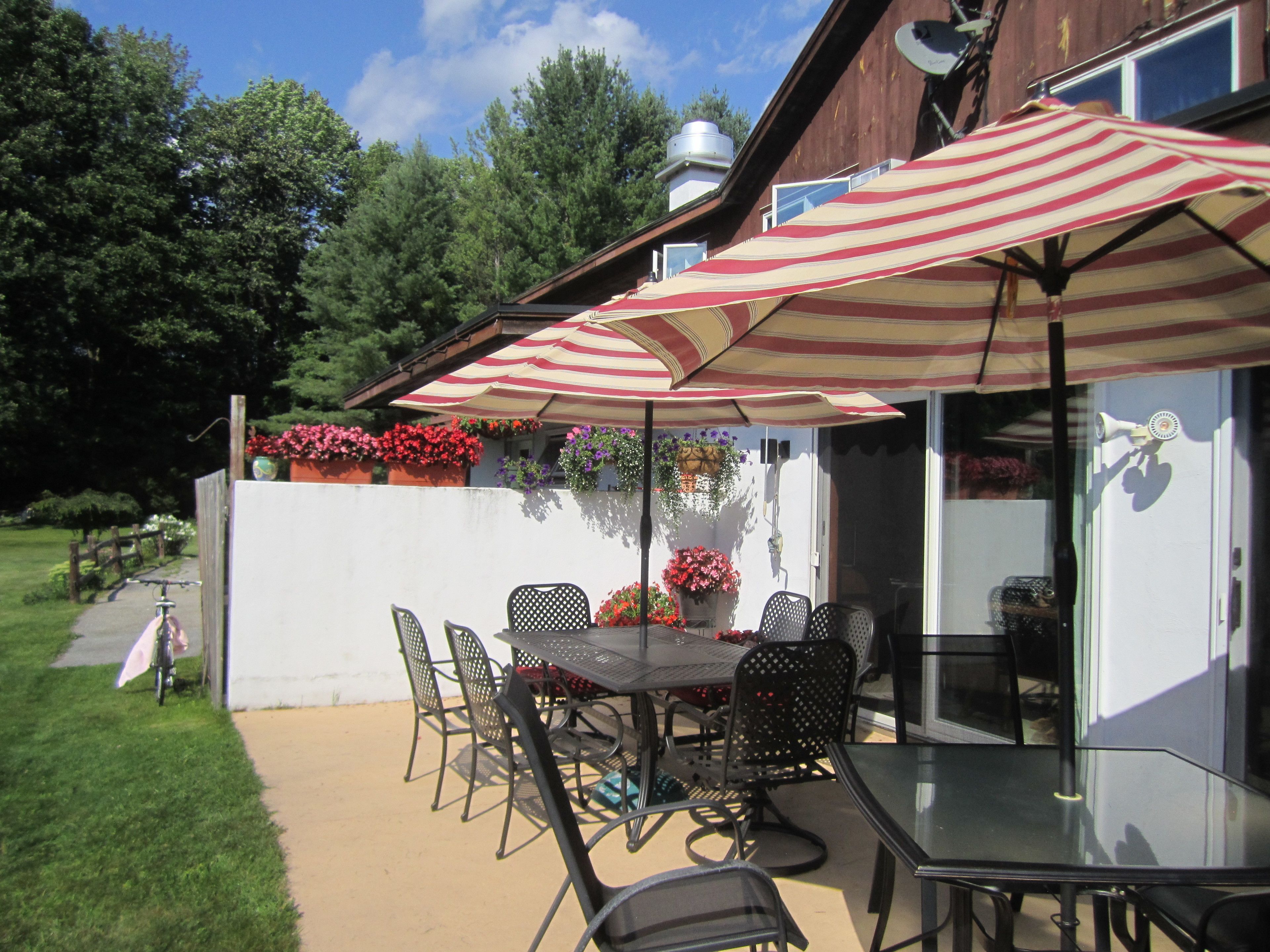 An outdoor patio with a table and chairs, a striped umbrella, and potted plants.