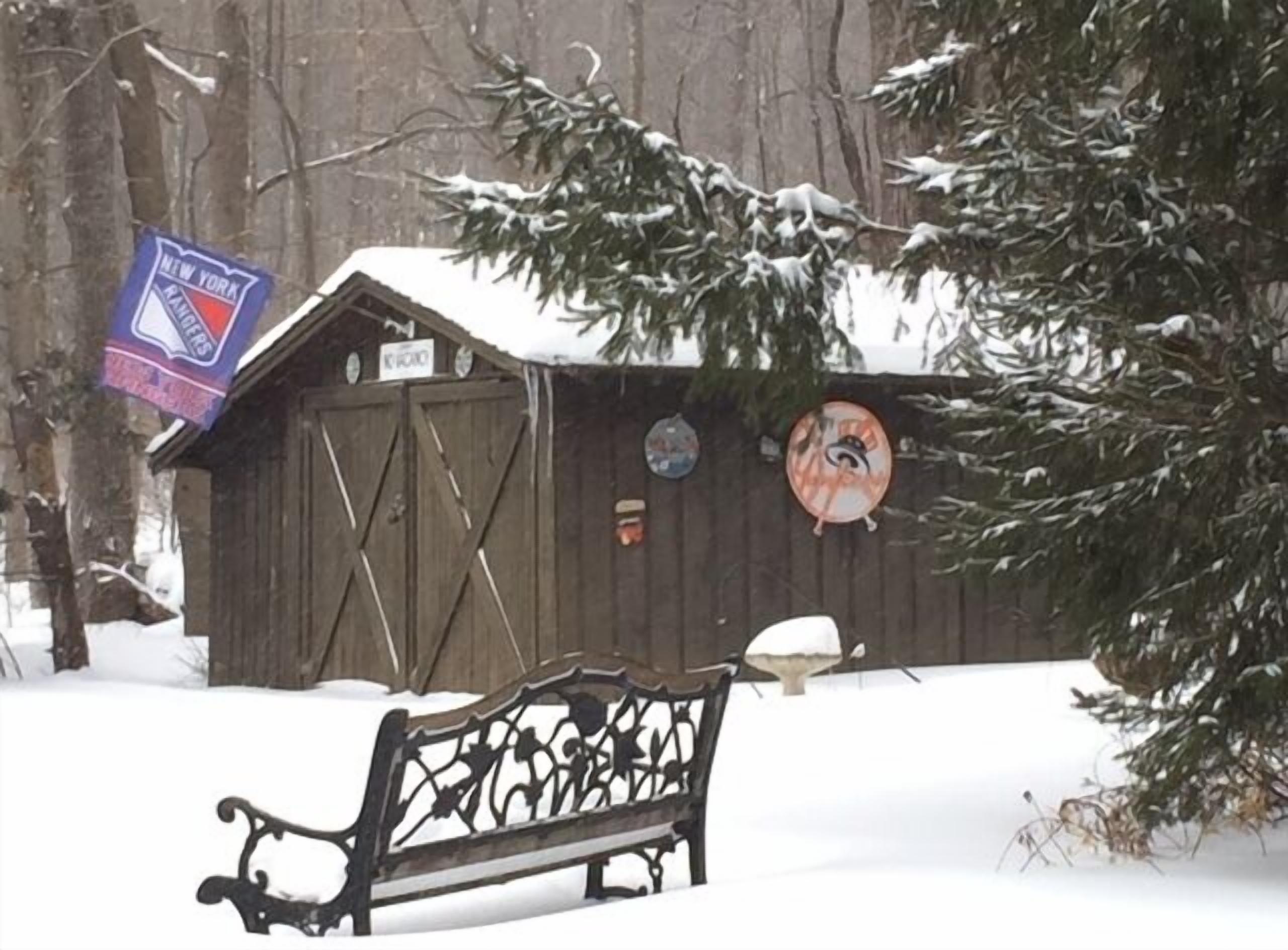 Eine Holzhütte mit schneebedecktem Dach, einer Bank davor und einem Schild, das anzeigt, dass es sich um einen Standort der New York Rangers handelt.