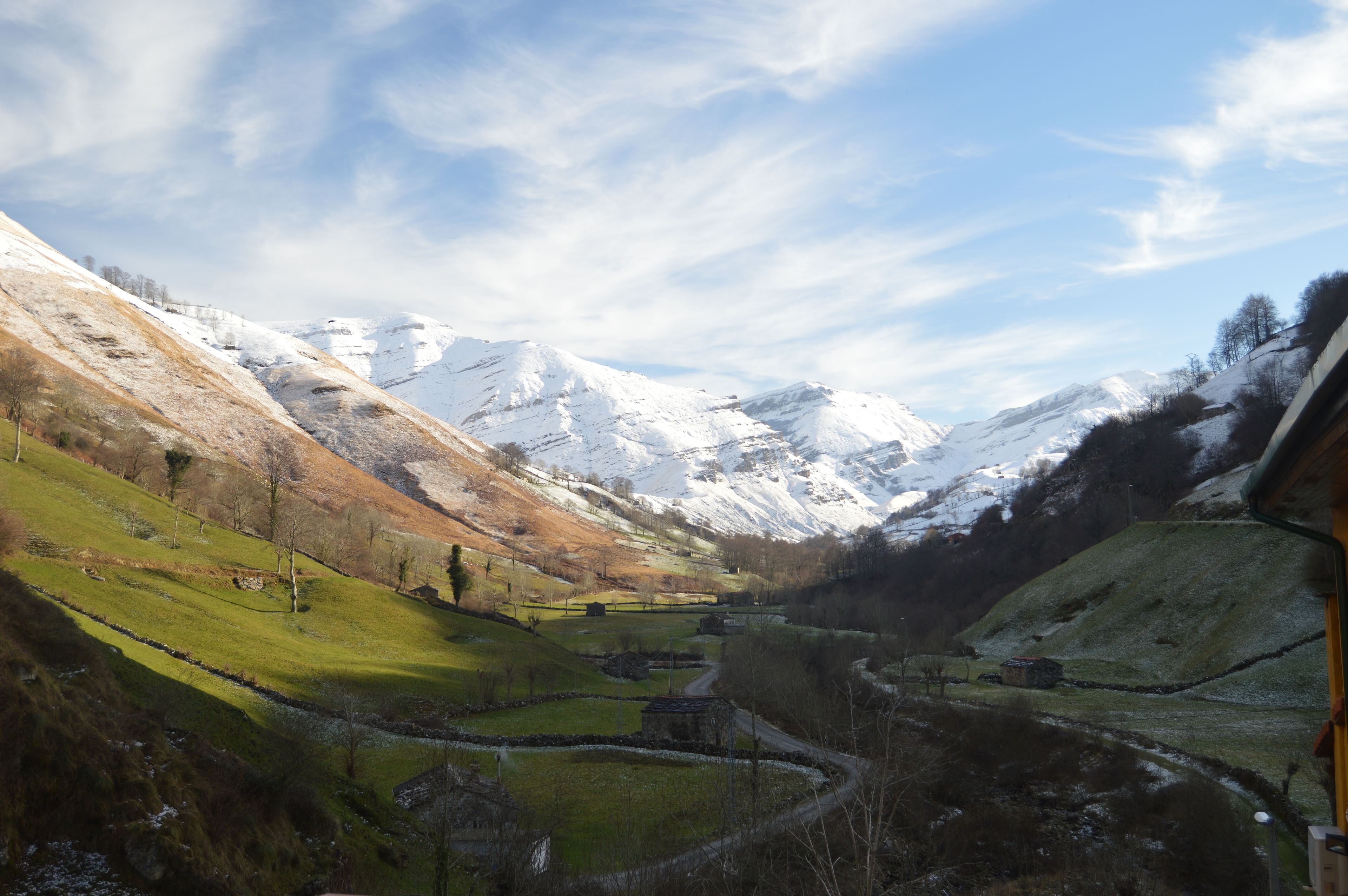 A mountainous landscape with snow-capped peaks, a winding road, and a few buildings.