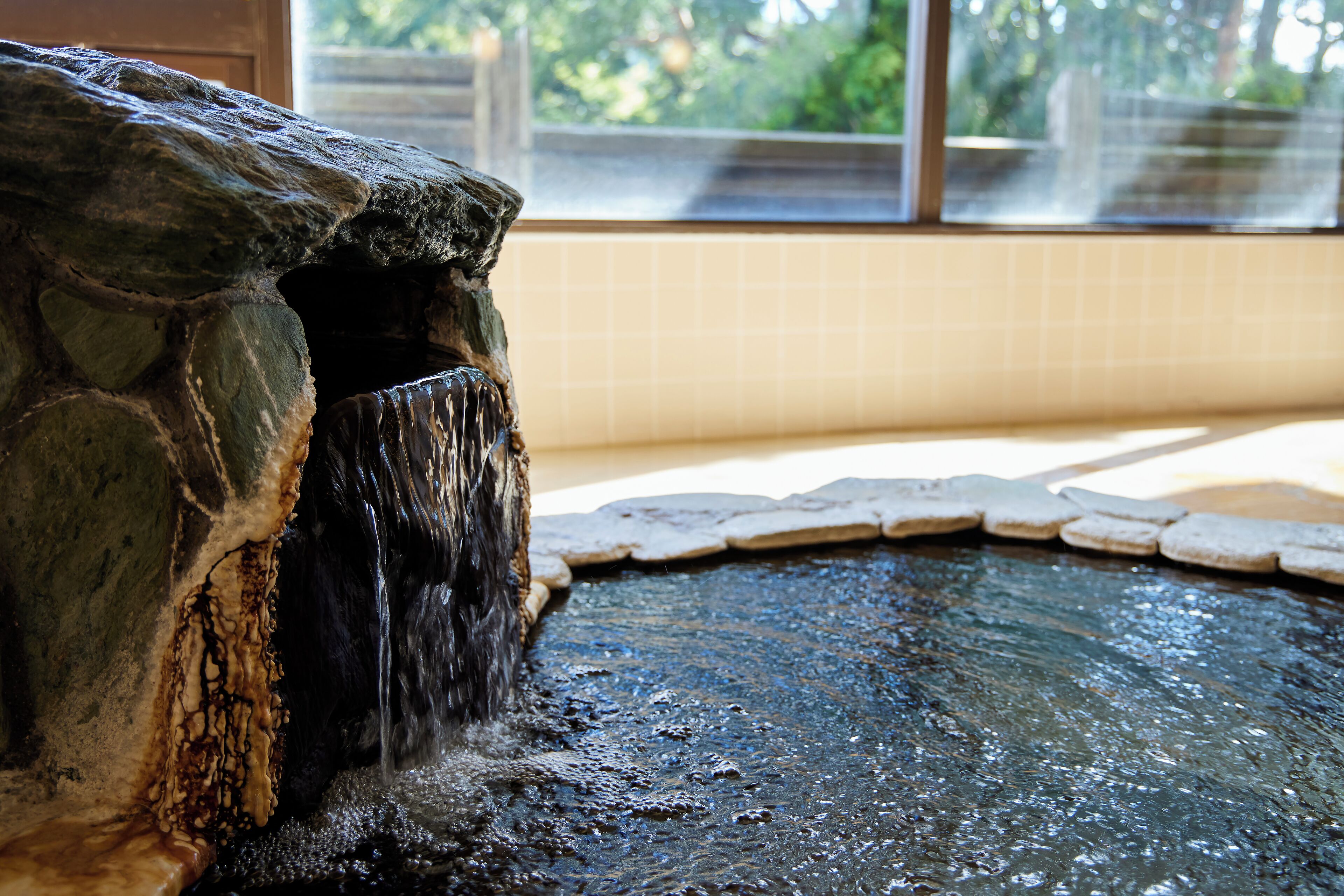A stone water feature with a cascading waterfall in a tiled area.