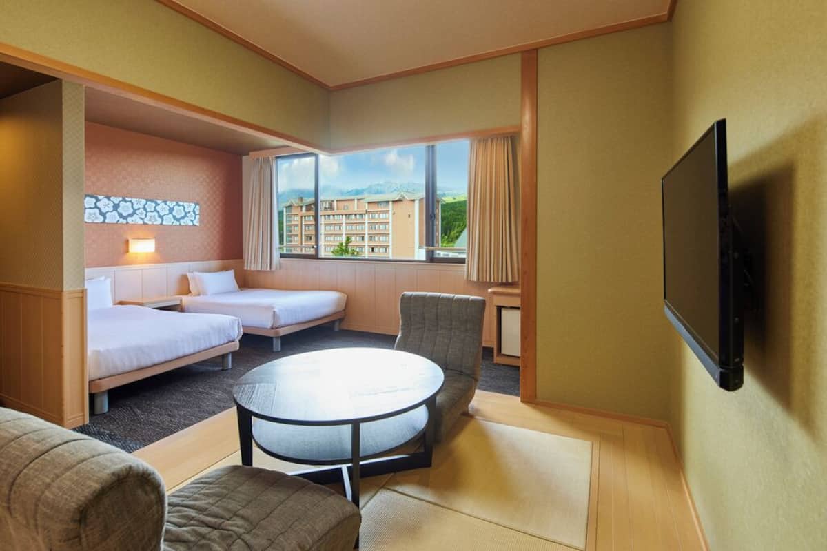 A hotel room with two beds, a round table, a TV, and a window with a view of buildings.