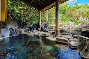 A tranquil outdoor hot spring area with a wooden structure, large rocks, and lush greenery. - Kamenoi Hotel Aso Park Resort (Aso)
