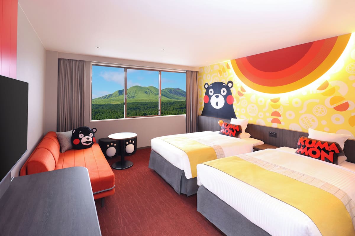 A hotel room with two beds, a sofa, a TV, and a large window with a mountain view.