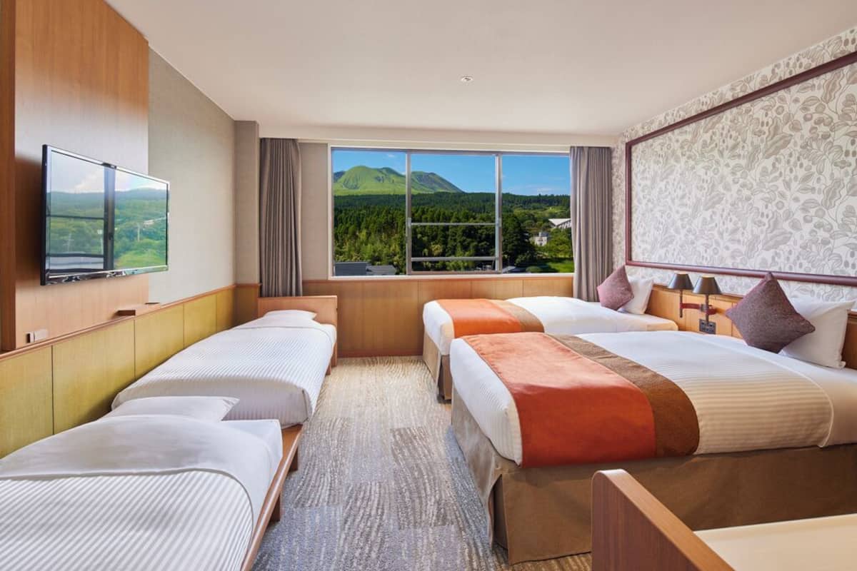 A hotel room with three beds, a TV, a large window with a mountain view, and a patterned wall.