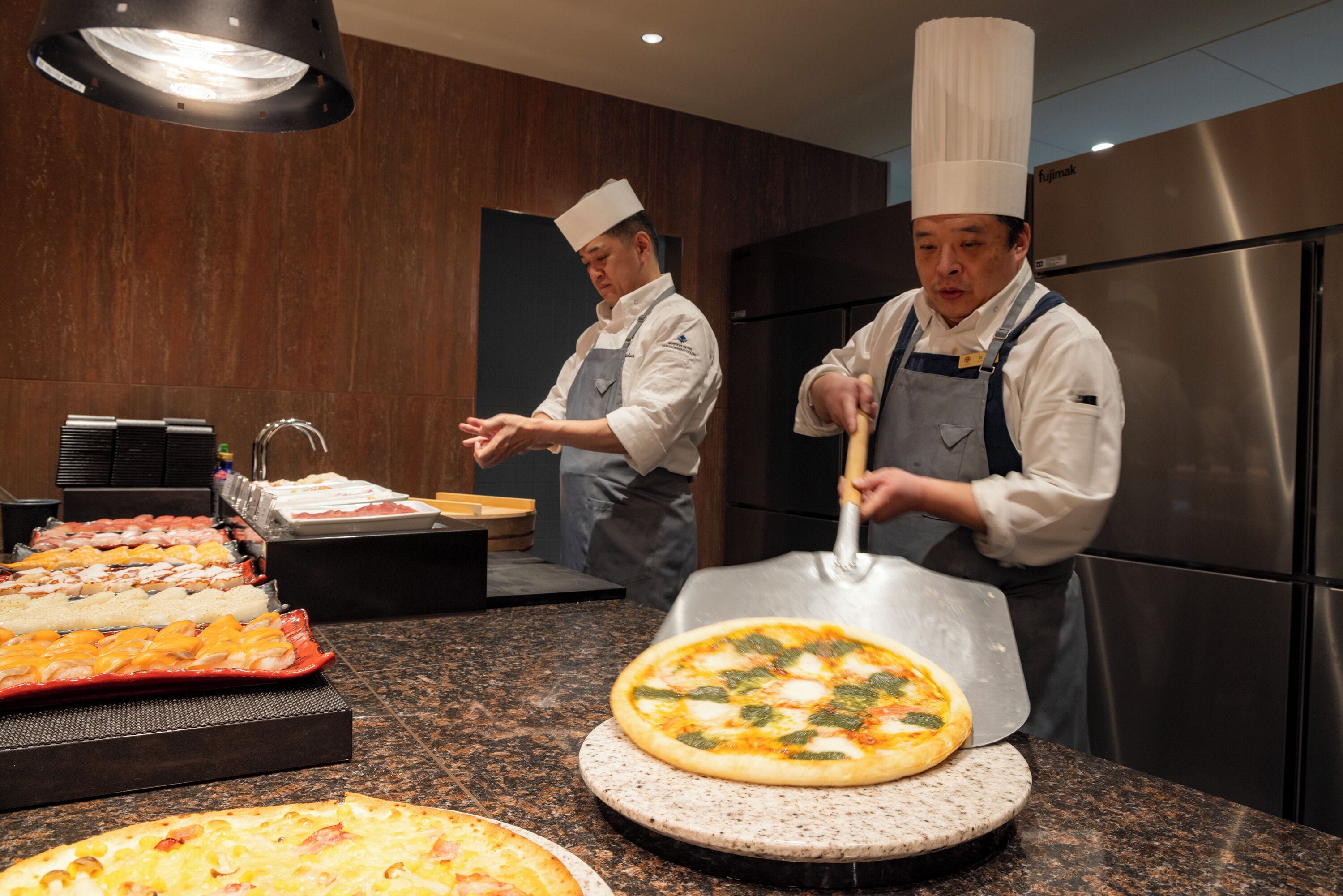 Köche bereiten Pizzen in einer modernen Küche mit Edelstahlgeräten und einer Marmorarbeitsplatte zu.