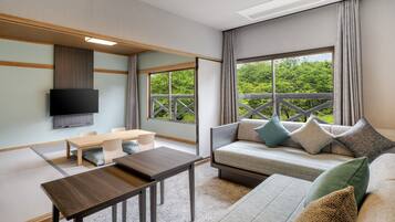 A modern room with a sofa, a TV mounted on the wall, a wooden table, and a view of greenery outside.