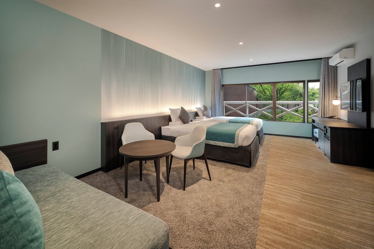 A modern hotel room with a bed, a seating area with a table, and a large window offering a view.