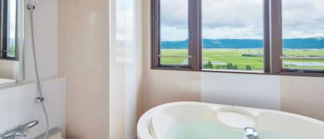 A bathroom with a bathtub, shower, and a window with a view of a green landscape.