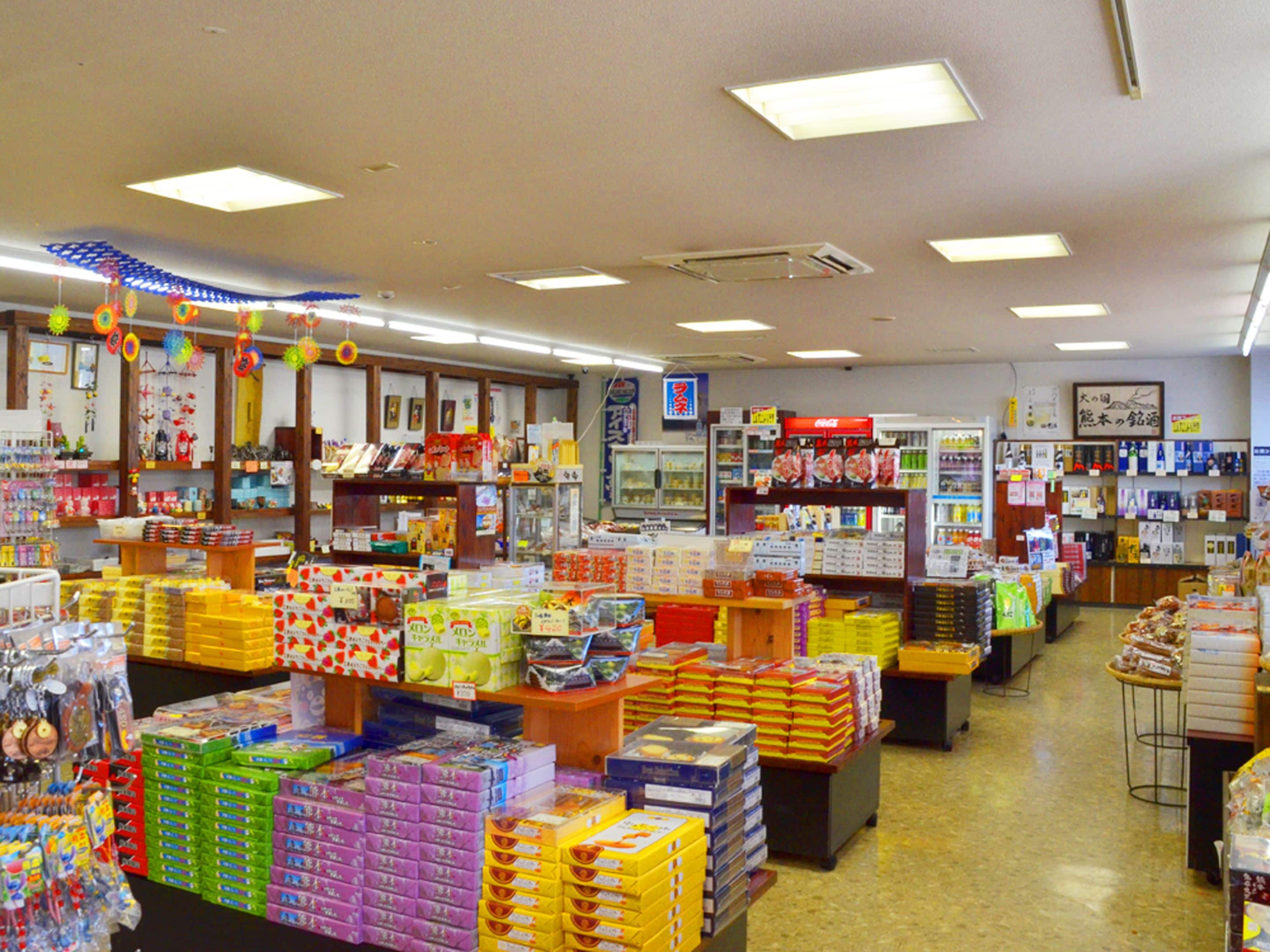 Una tienda de conveniencia muy iluminada con varios productos en estantes y recipientes, incluyendo bocadillos, bebidas y artículos para el hogar.
