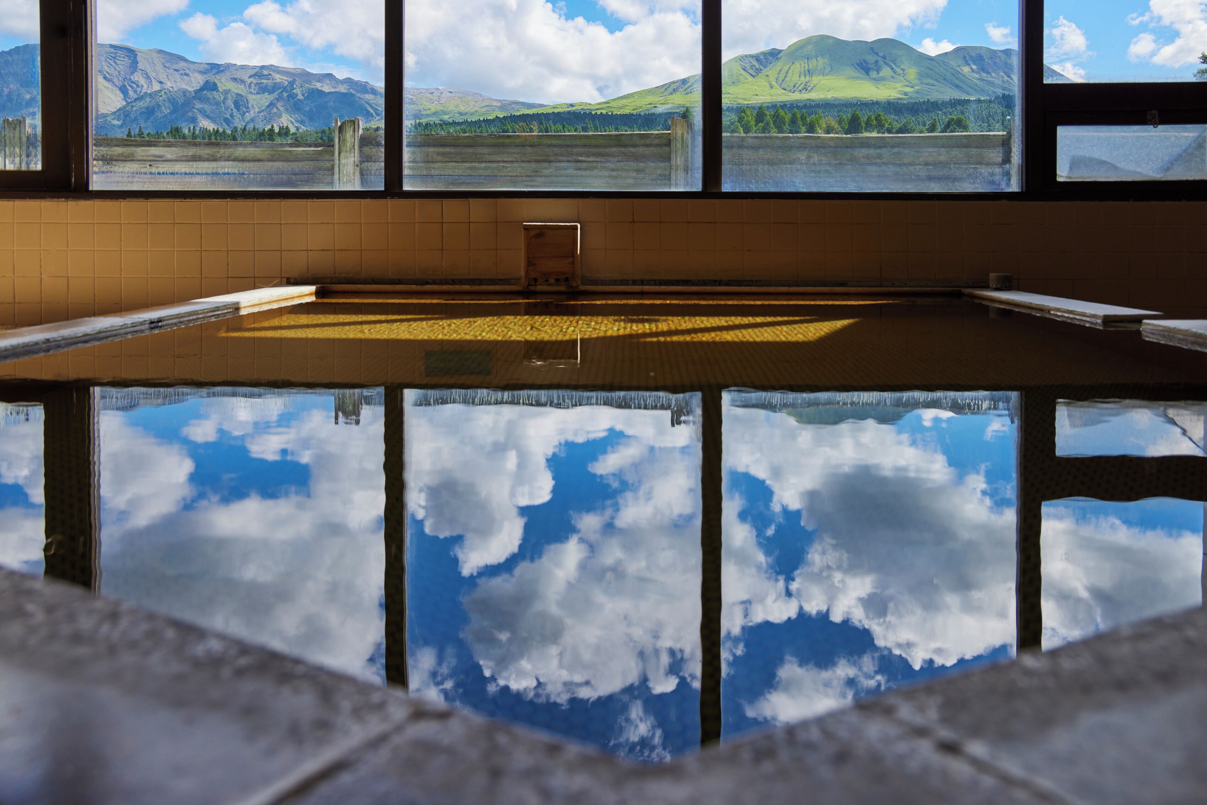 Ein Schwimmbad mit Blick auf Berge und einen See durch große Fenster.