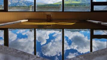 Ein Schwimmbad mit Blick auf Berge und einen See durch große Fenster.