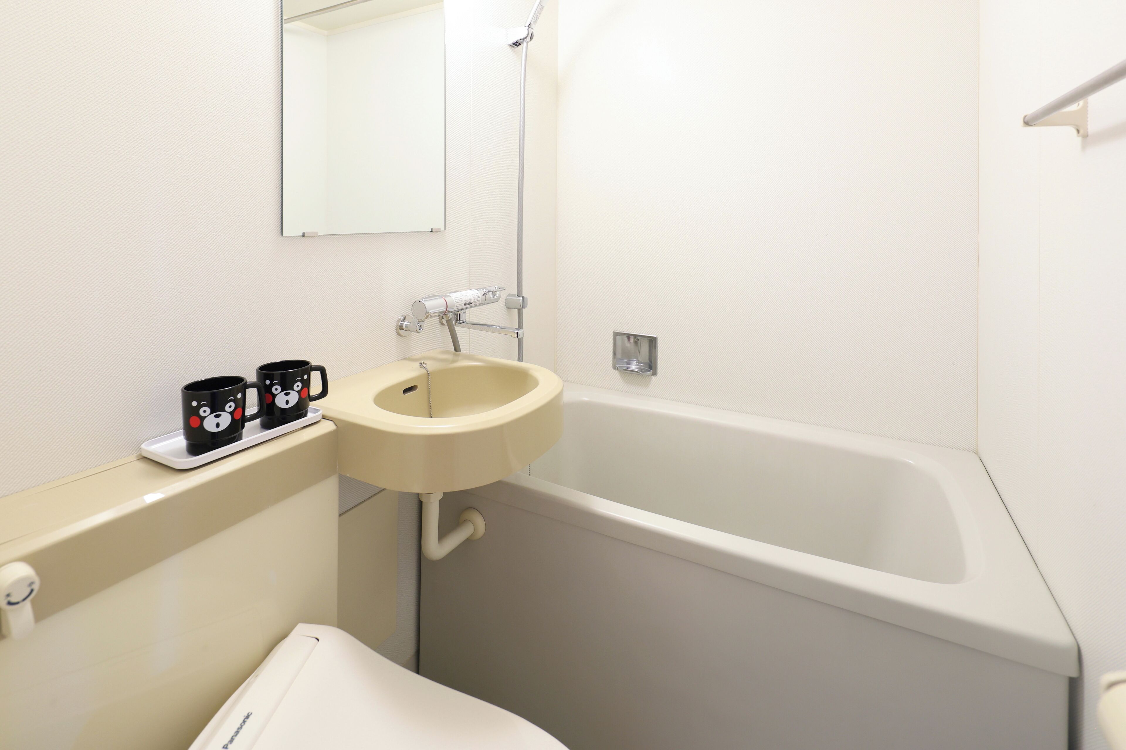 A bathroom with a bathtub, a sink, and a mirror. There are two mugs on the counter.