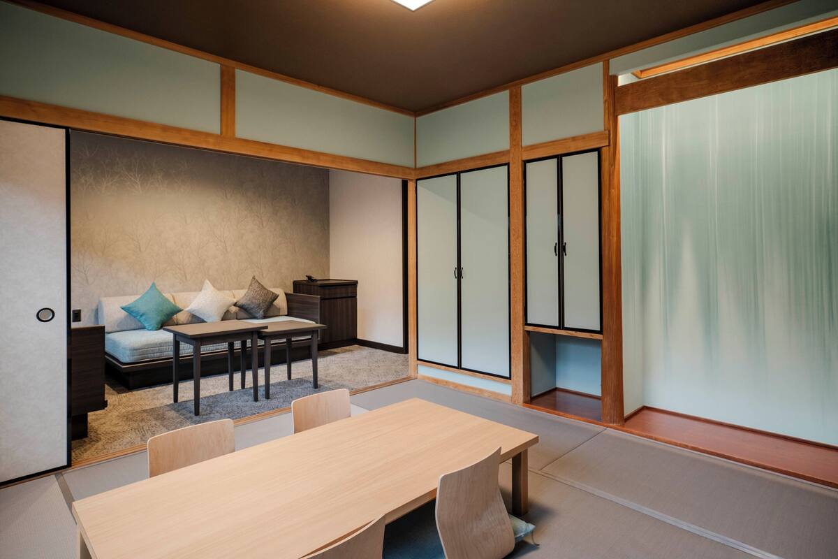 A traditional Japanese-style room with tatami flooring, a low table, a sofa with cushions, and sliding doors.
