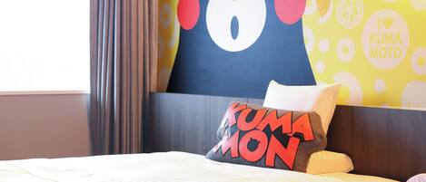 Una habitación de hotel con una cama, un almohadón con la inscripción 'KUMA MOTO' y una pared con un diseño de oso y la leyenda 'I ♥ KUMA MOTO'.