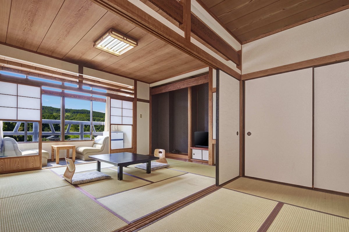 A traditional Japanese room with tatami flooring, a low table, a sofa, and a television.