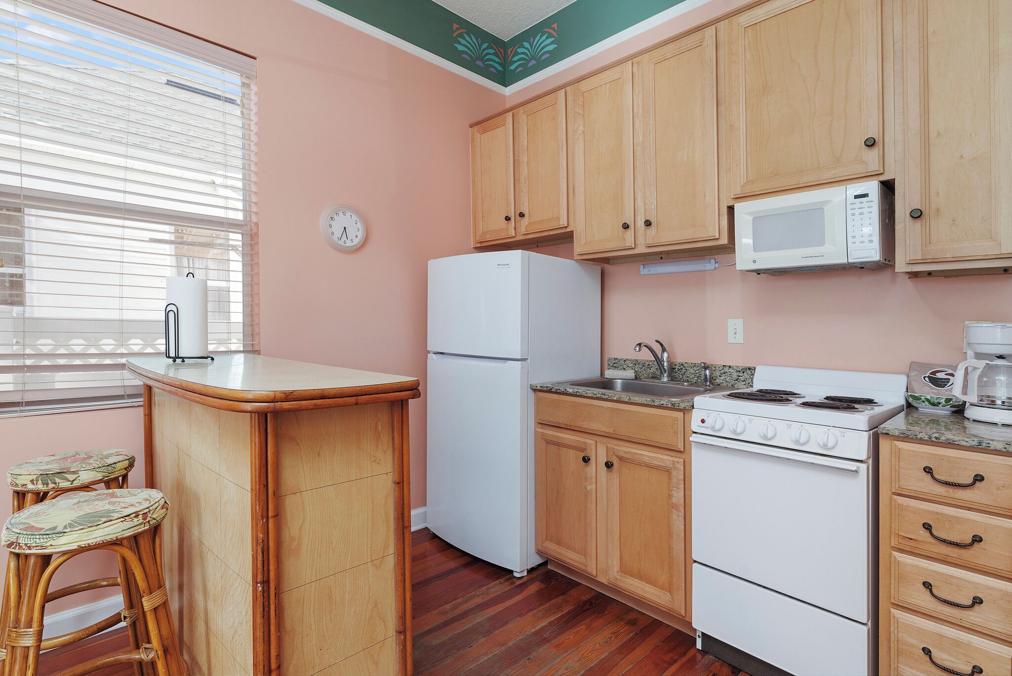 Una cocina con armarios de madera, un refrigerador blanco, una estufa y un microondas. Hay dos taburetes en la barra.