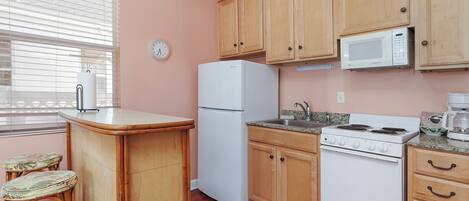 Una cocina con armarios de madera, un refrigerador blanco, una estufa y un microondas. Hay dos taburetes en la barra.