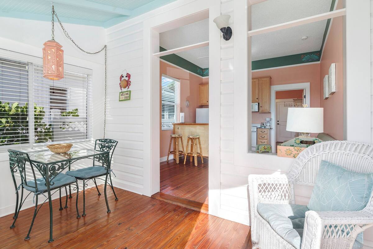 A dining area with a table and chairs, a wicker chair, and a view into the kitchen.