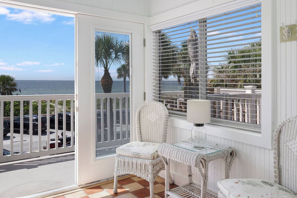 A balcony with wicker furniture, a glass table, and a view of the ocean.