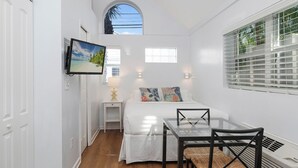 Un dormitorio con cama, mesita de noche, lámpara y televisor montado en la pared.