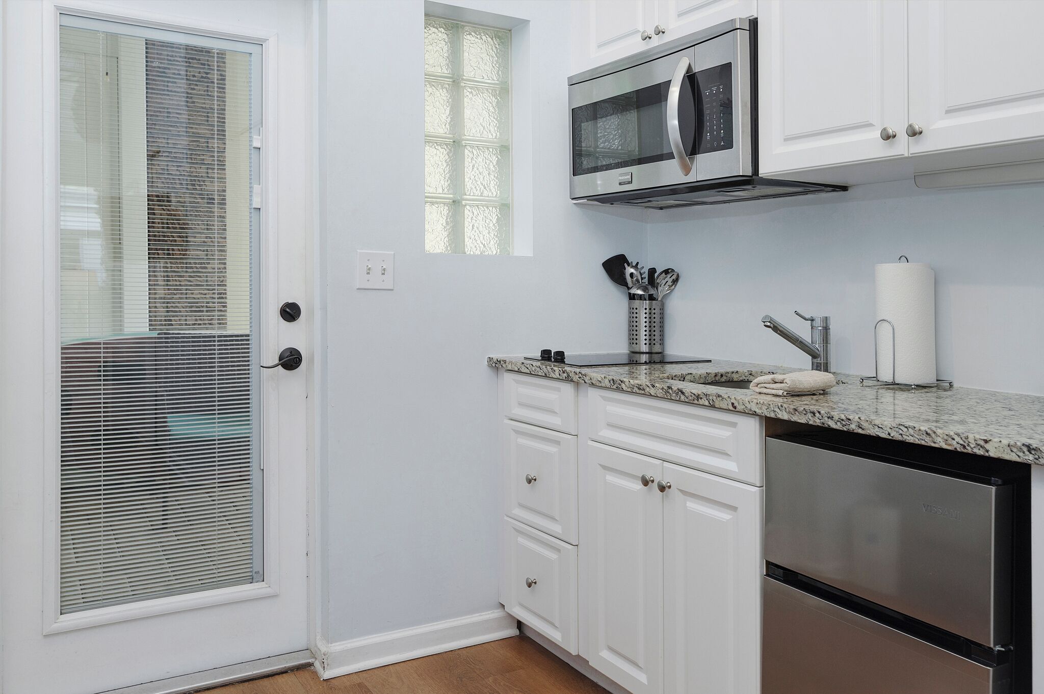 Una cocina con gabinetes blancos, un microondas de acero inoxidable y un lavavajillas.