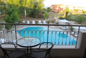 A balcony with a view of a swimming pool, lounge chairs, and potted plants. - Toni's Guesthouse (Corfu)