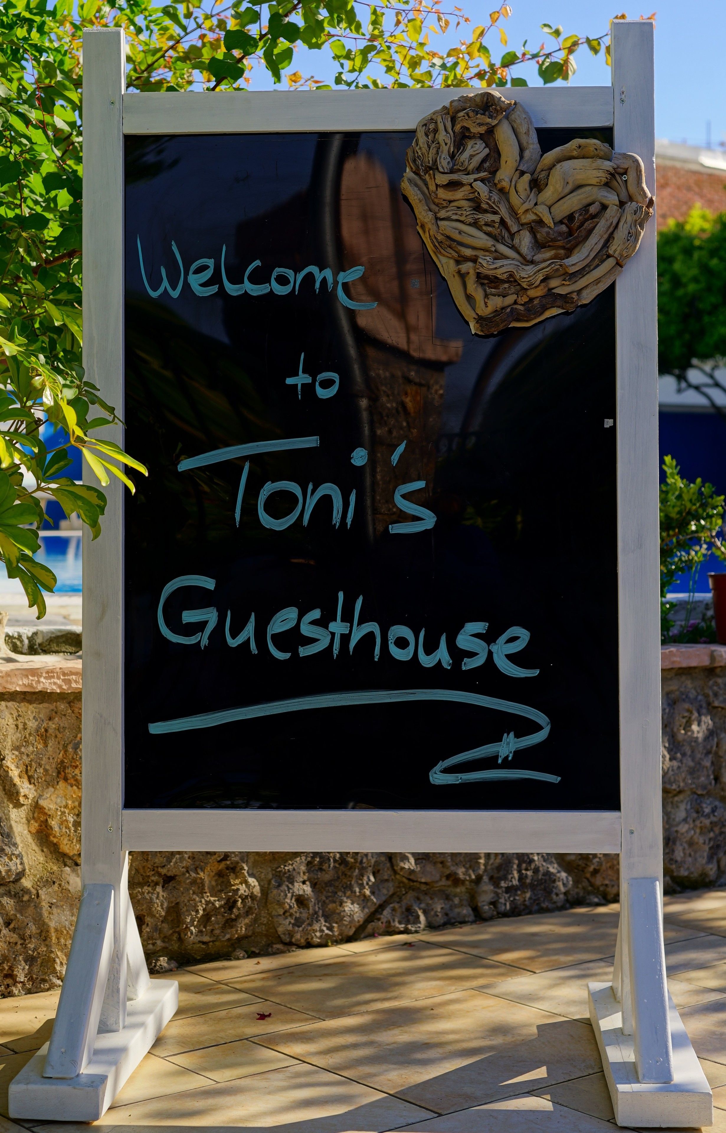 Eine schwarze Tafel mit der Aufschrift 'Welcome to Toni's Guesthouse' in blauer Kreide.