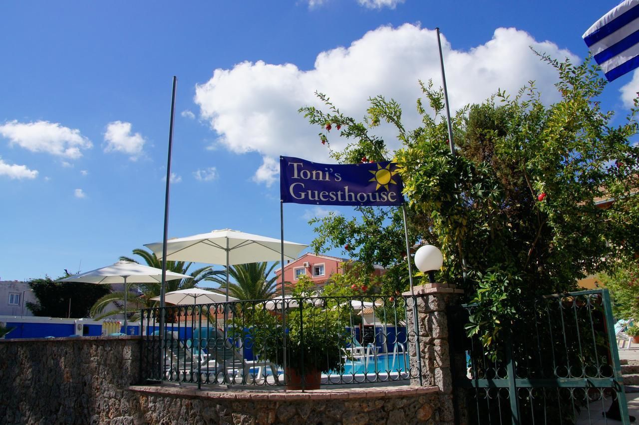 A sign for Toni's Guesthouse with a pool area in the background.