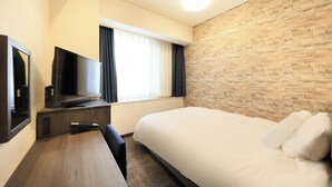 A hotel room with a bed, a desk with a flat-screen TV, a window with curtains, and a brick-patterned wall. - Hotel Nagano Avenue (Nagano)
