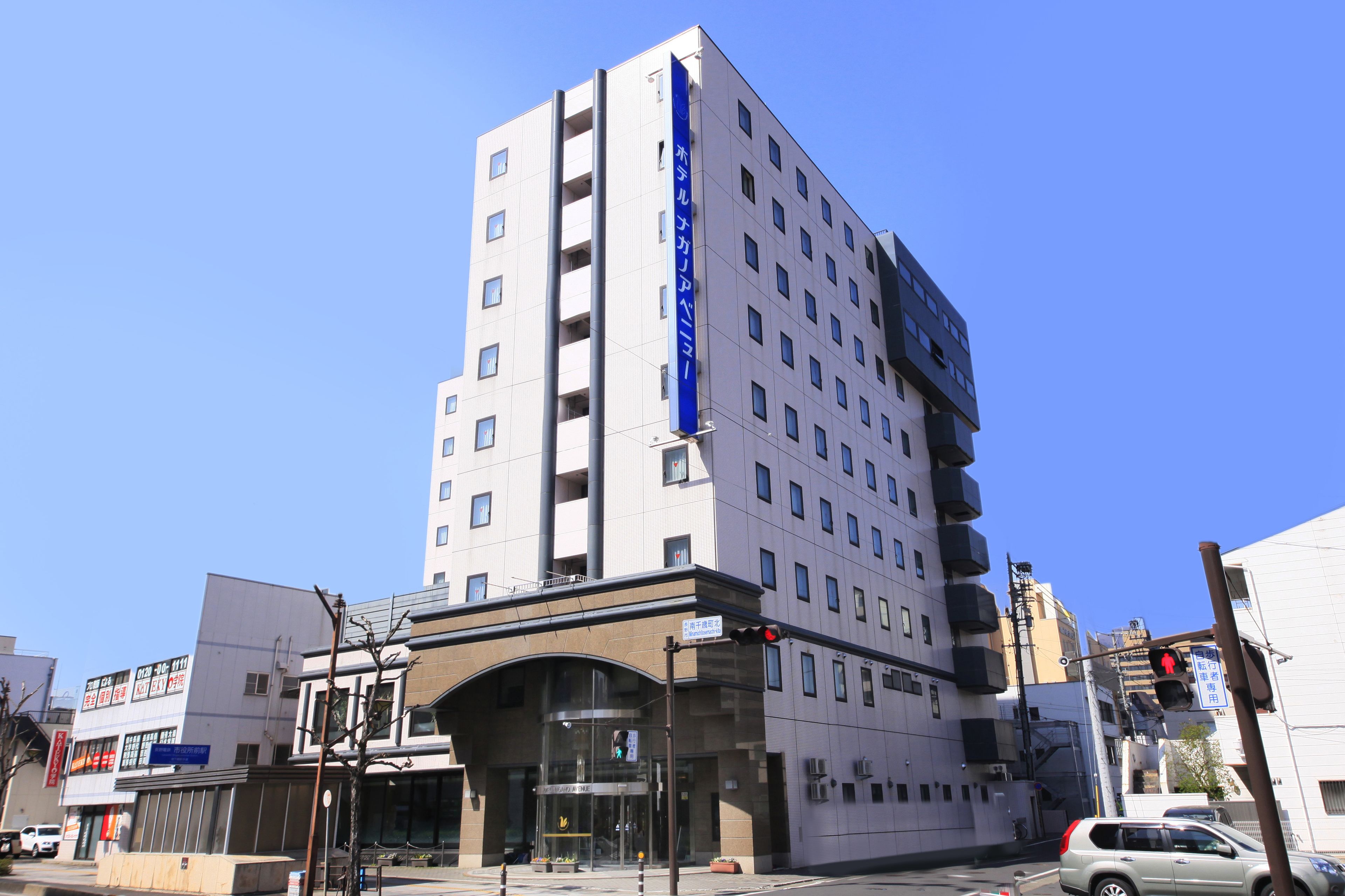 Een hotel met meerdere verdiepingen, met een opvallend blauw bord op de gevel, een ruime entree met een glazen overkapping en verschillende balkons.