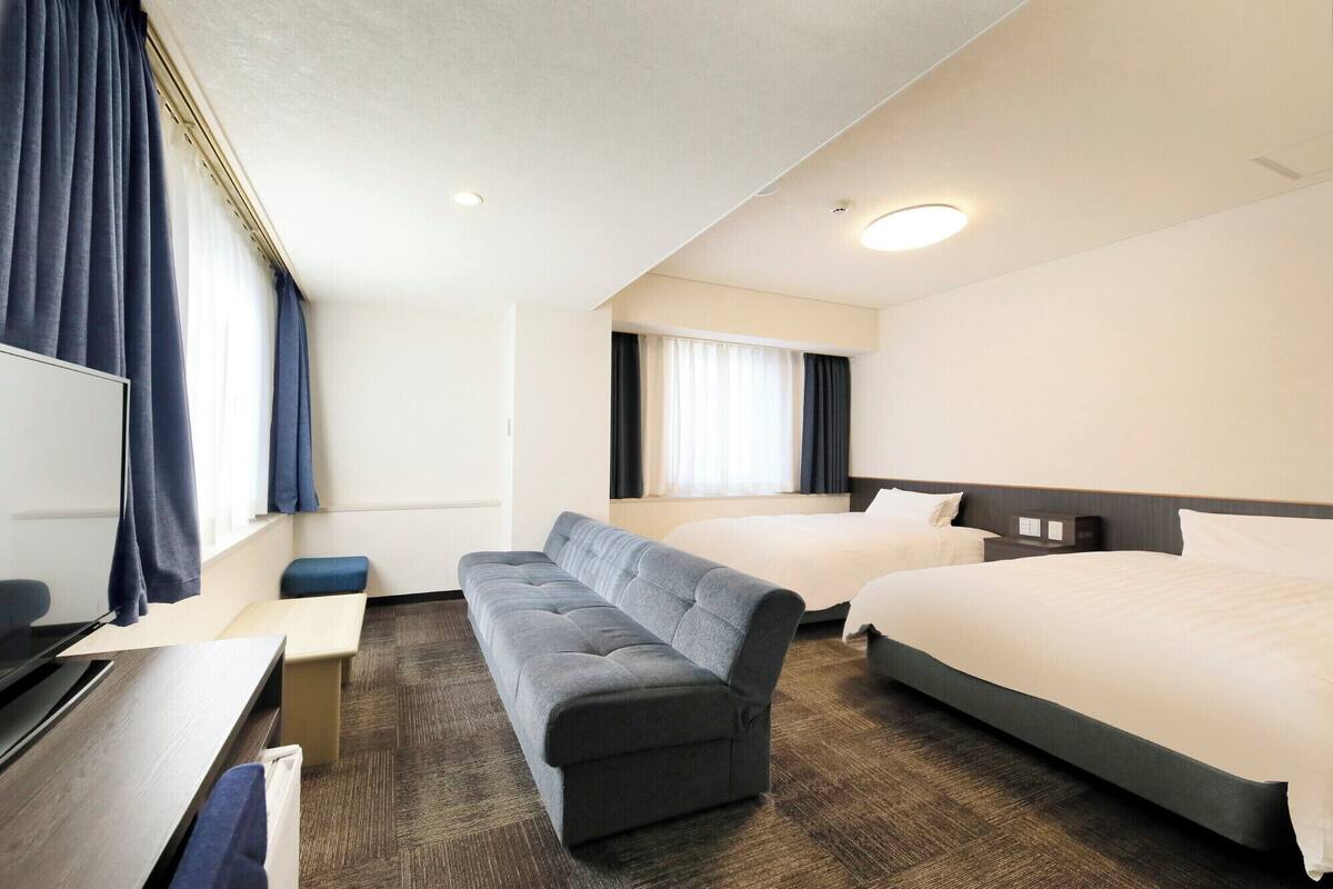 Habitación de hotel con dos camas, un sofá, un escritorio y una ventana con cortinas.