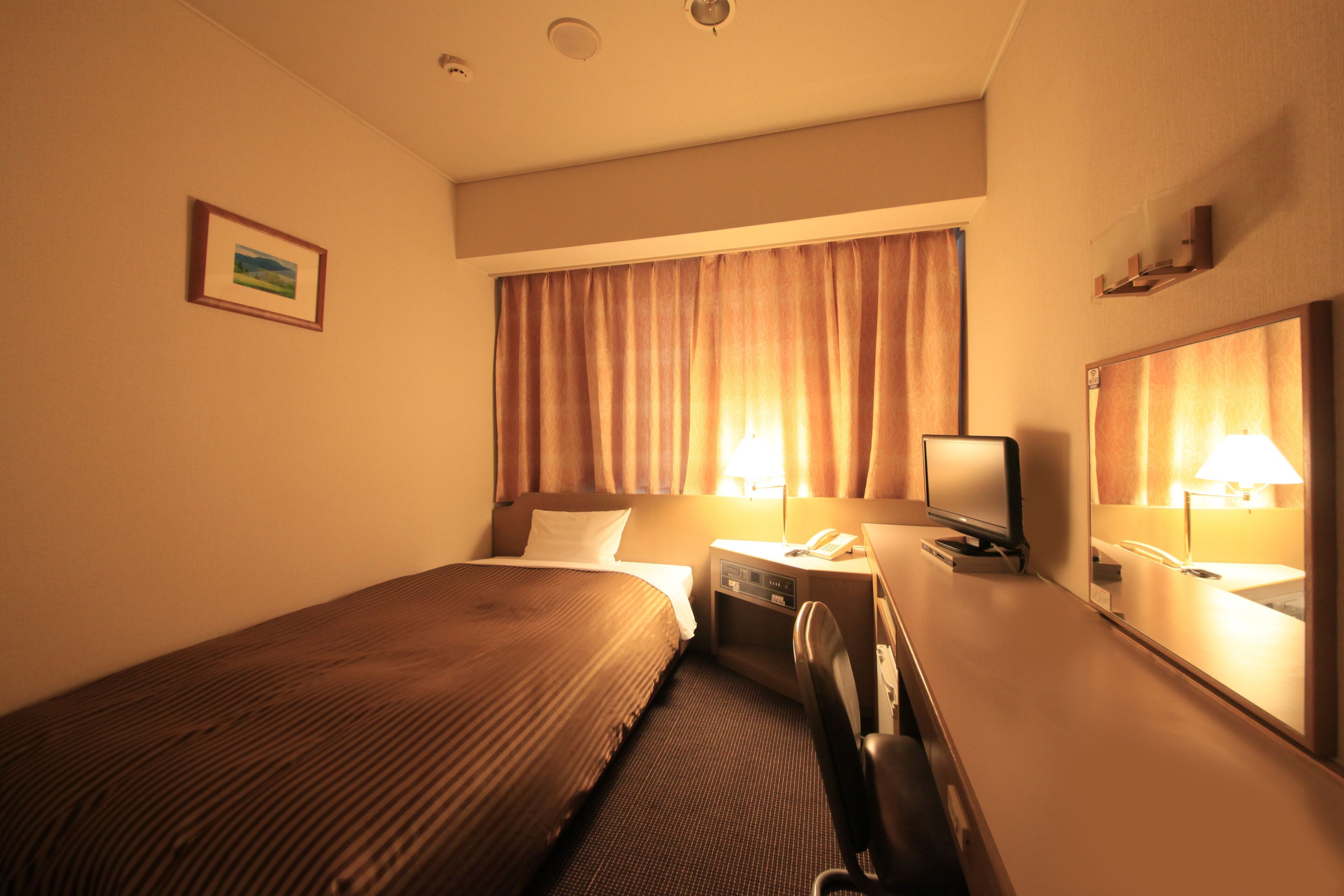 Quarto de hotel com cama, escrivaninha, cadeira, telefone e espelho.