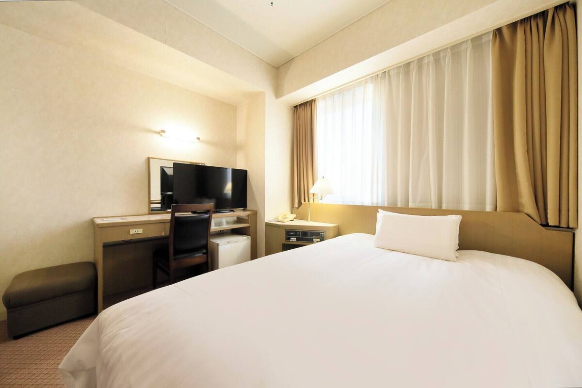 Una habitación de hotel con cama, escritorio con televisor, silla, lámpara y teléfono.
