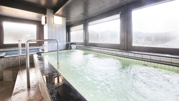 An indoor swimming pool with clear glass walls, a metal ladder, and a view of distant buildings. - Hotel Nagano Avenue (Nagano)