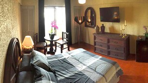 A bedroom with a bed, dresser, vanity, and a small table with a lamp. - Aurora Suites (Guadalajara)