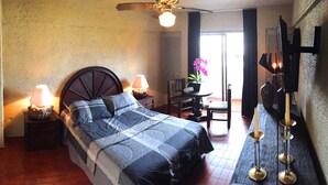A bedroom with a bed, bedside lamps, a small table with a potted plant, and a wall-mounted light fixture. - Aurora Suites (Guadalajara)