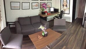 A modern office space with a grey sofa, a wooden table with a vase of flowers, and framed certificates on the wall. - Aurora Suites (Guadalajara)